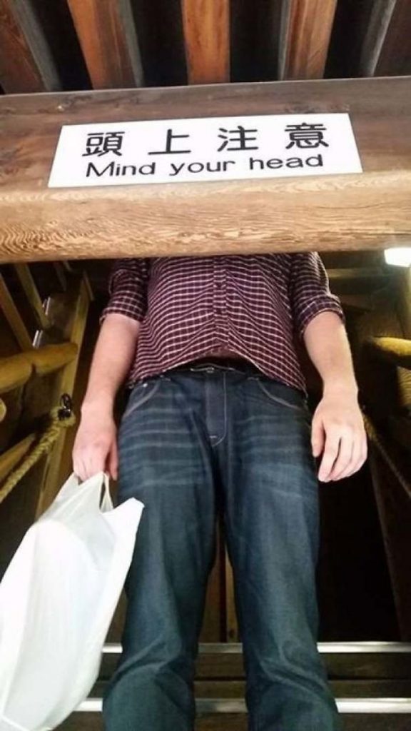 A Man Standing Behind a Sign that Reads ‘Mind Your Head’
